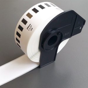 Brother DK-22210 continuous paper label roll front view Brother DK-22210 showing white roll with black print Brother DK-22210 roll installed in a Brother QL printer Brother DK-22210 printing custom-length labels Brother DK-22210 close-up on printed label surface Brother DK-22210 roll alongside packaging box